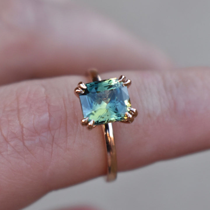 A hand holding a Parti Sapphire Solitaire Engagement Ring with double claw prongs, with a rose gold band.